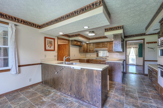 2010 Hartland Rd, Franklin, TN 37069 - kitchen with a textured ceiling, a peninsula, under cabinet range hood, brown cabinets, and stainless steel gas cooktop