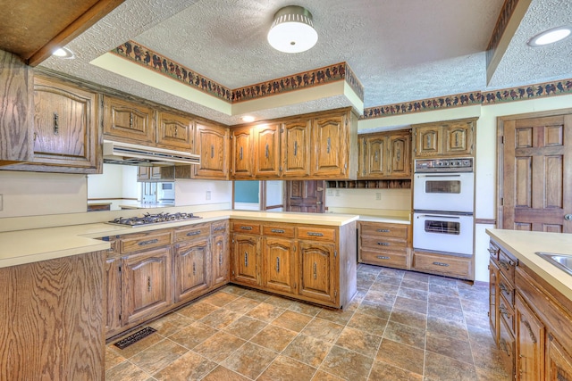 2010 Hartland Rd, Franklin, TN 37069 - kitchen featuring double oven, stainless steel gas cooktop, under cabinet range hood, brown cabinets, and a textured ceiling