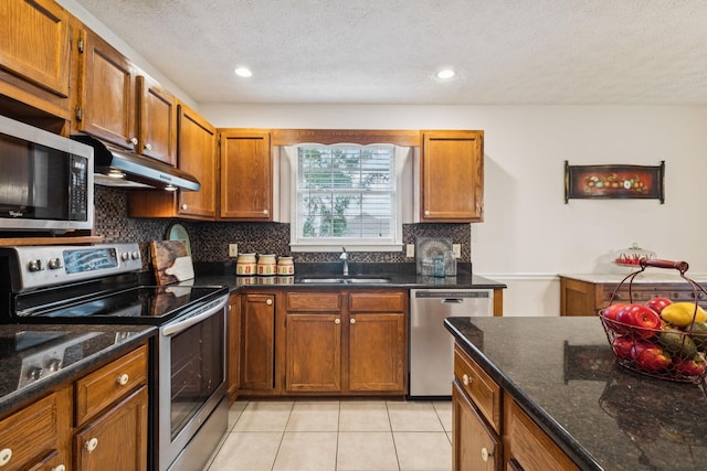 217 Fox Hunt Ln, Lebanon, TN 37087 - kitchen with appliances with stainless steel finishes, under cabinet range hood, tasteful backsplash, brown cabinetry, and a textured ceiling