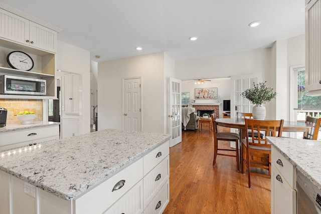 513 Foxcroft Cir, Franklin, TN 37067 - kitchen with stainless steel microwave, a fireplace, a ceiling fan, wood finished floors, and white cabinetry