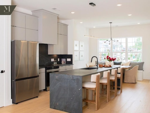 1572 Madison St, Chattanooga, TN 37408 - kitchen featuring stainless steel appliances, dark countertops, light wood-style flooring, decorative backsplash, and a breakfast bar