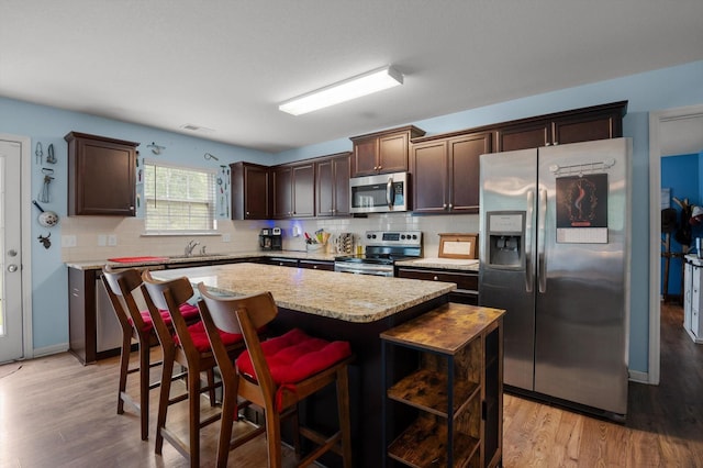15252 Foamflower Ln, Sale Creek, TN 37373 - kitchen featuring appliances with stainless steel finishes, dark brown cabinetry, a center island, light wood finished floors, and decorative backsplash