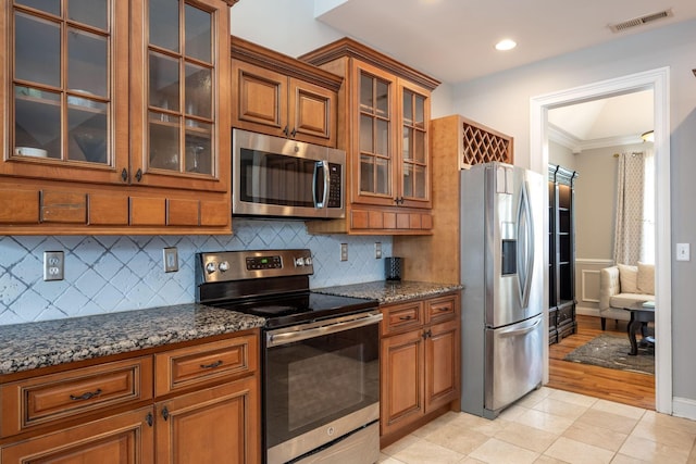 6853 Manassas Gap Ln, Hixson, TN 37343 - kitchen with appliances with stainless steel finishes, brown cabinets, crown molding, dark stone countertops, and glass insert cabinets