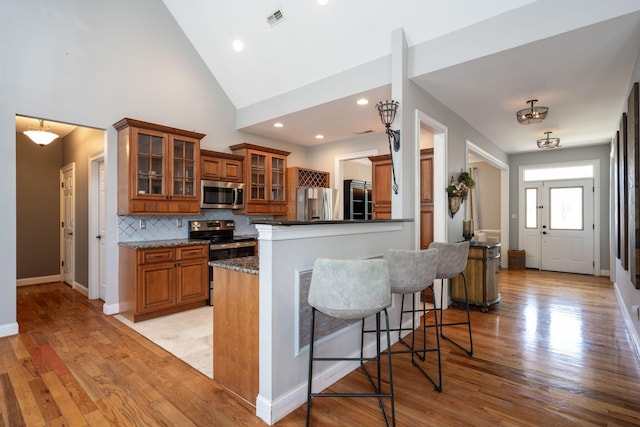 6853 Manassas Gap Ln, Hixson, TN 37343 - kitchen featuring stainless steel appliances, brown cabinetry, tasteful backsplash, light wood-style flooring, and high vaulted ceiling