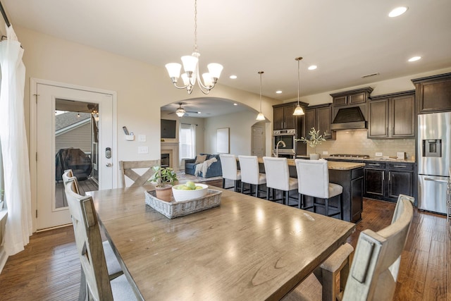 222 Fowler Cir, Franklin, TN 37064 - dining room with a ceiling fan, arched walkways, a chandelier, a fireplace, and dark wood-style flooring