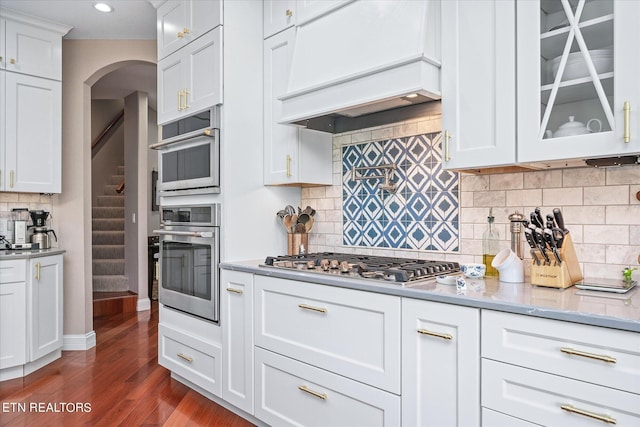 145 Pineridge Loop, Crossville, TN 38558 - kitchen featuring appliances with stainless steel finishes, custom range hood, dark wood-style flooring, glass insert cabinets, and tasteful backsplash
