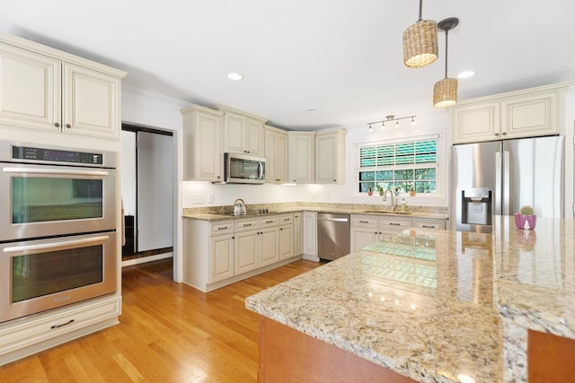 5033 Ragland Dr, Nashville, TN 37220 - kitchen featuring appliances with stainless steel finishes, cream cabinetry, light stone countertops, light wood-type flooring, and hanging light fixtures