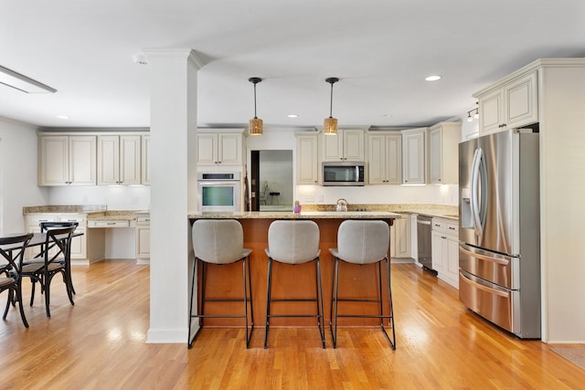 5033 Ragland Dr, Nashville, TN 37220 - kitchen with stainless steel appliances, a breakfast bar, cream cabinetry, light wood-style floors, and recessed lighting