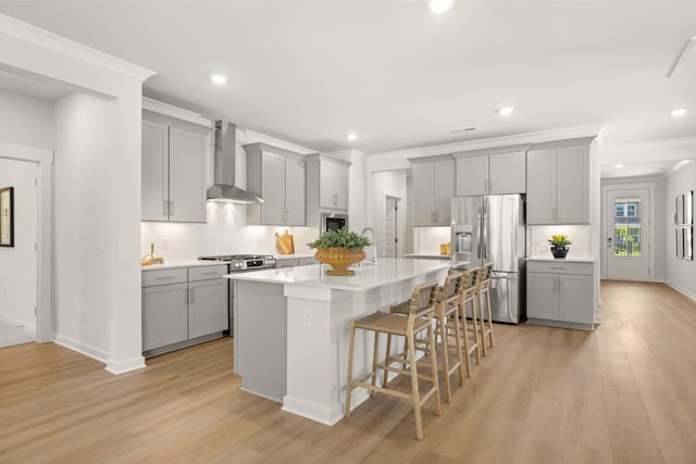 2453 Williams Ridge Dr, Columbia, TN 38401 - kitchen with gray cabinetry, appliances with stainless steel finishes, wall chimney exhaust hood, a breakfast bar, and light wood finished floors