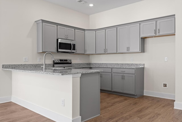 212 Mcbrien Rd, Chattanooga, TN 37411 - kitchen with stainless steel appliances, gray cabinets, a peninsula, light stone countertops, and wood finished floors