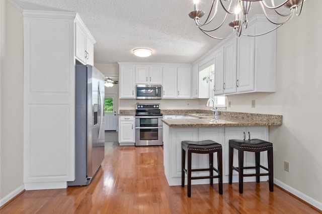 435 Forest St, Lewisburg, TN 37091 - kitchen featuring appliances with stainless steel finishes, a peninsula, white cabinets, a chandelier, and a textured ceiling