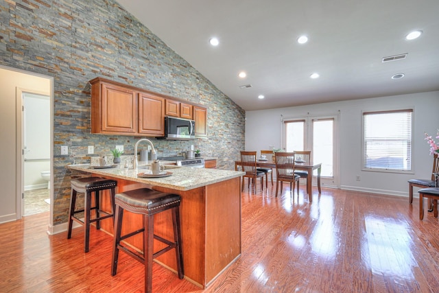 1005 Lark Ct, Spring Hill, TN 37174 - kitchen with appliances with stainless steel finishes, light stone counters, brown cabinets, high vaulted ceiling, and light wood-style floors