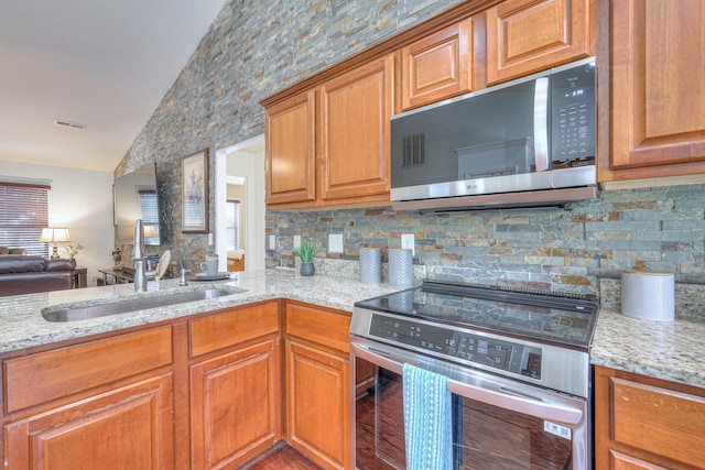 1005 Lark Ct, Spring Hill, TN 37174 - kitchen with stainless steel microwave, range, vaulted ceiling, light stone countertops, and brown cabinetry