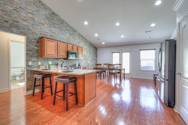 1005 Lark Ct, Spring Hill, TN 37174 - kitchen featuring stainless steel appliances, light stone counters, a peninsula, brown cabinetry, and light wood-style flooring
