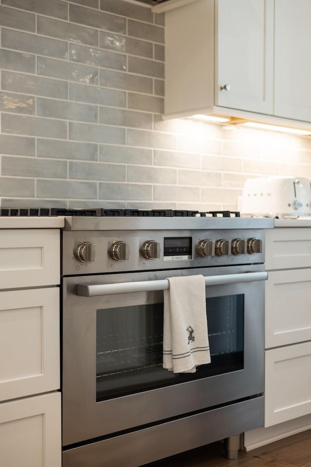 7019 Bolton St, Franklin, TN 37064 - kitchen featuring stainless steel stove, decorative backsplash, white cabinetry, and wood finished floors