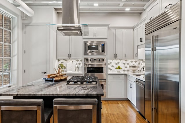 320 Liberty Pike Unit 205, Franklin, TN 37064 - kitchen featuring built in appliances, island exhaust hood, tasteful backsplash, light wood-style floors, and stone counters