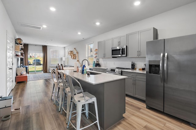 622 Birdie Dr, Spring Hill, TN 37174 - kitchen featuring stainless steel appliances, gray cabinetry, an island with sink, a kitchen bar, and light wood finished floors