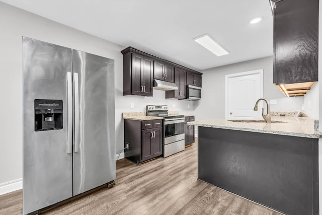 626 Snowshoe Ln, Clarksville, TN 37040 - kitchen with stainless steel appliances, under cabinet range hood, light wood-style flooring, light stone counters, and dark brown cabinetry