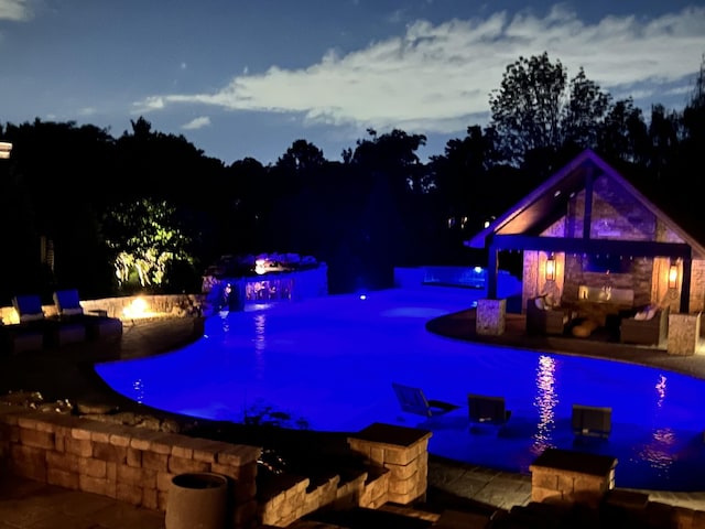 1300 Stovall Ln, Mount Juliet, TN 37122 - pool at night featuring a pool with connected hot tub, a patio area, and an outdoor living space with a fireplace