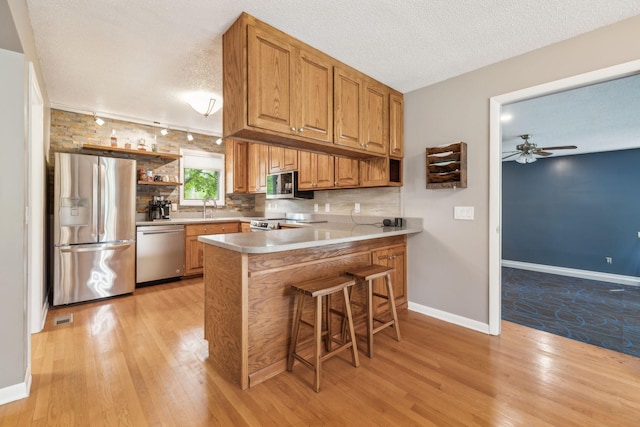 2261 High Meadow Dr, Murfreesboro, TN 37129 - kitchen with open shelves, stainless steel appliances, light wood-type flooring, a ceiling fan, and a peninsula