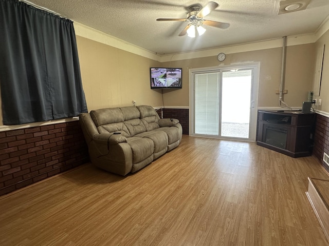 638 Chitwood Dr, Lafayette, TN 37083 - living room featuring a textured ceiling, light wood-style flooring, ceiling fan, brick wall, and a wainscoted wall