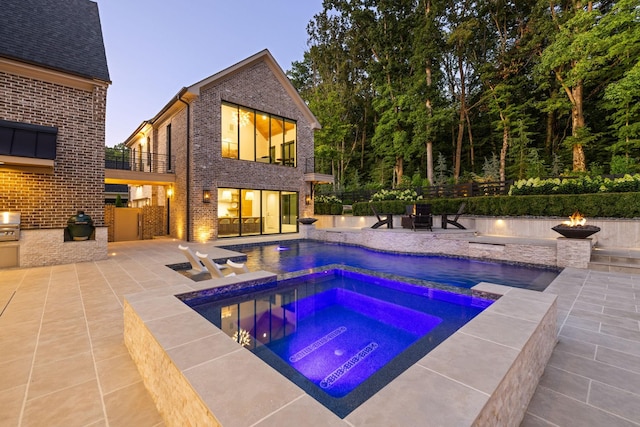 8524 Heirloom Blvd, College Grove, TN 37046 - pool at dusk featuring a fire pit, an outdoor kitchen, a patio, and a pool with connected hot tub
