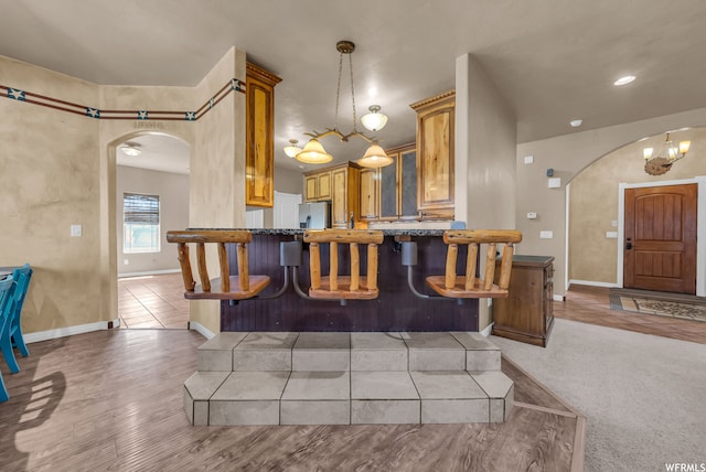 kitchen with kitchen peninsula, hanging light fixtures, light carpet, a kitchen bar, and stainless steel refrigerator with ice dispenser