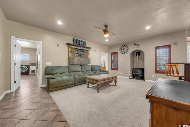 carpeted living room featuring ceiling fan, a wood stove, washer / dryer, and a healthy amount of sunlight