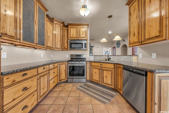 kitchen featuring decorative light fixtures, light tile flooring, dark stone counters, appliances with stainless steel finishes, and sink