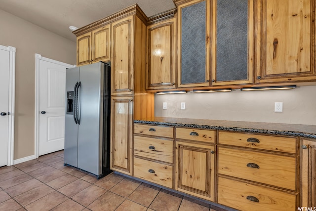 kitchen with light tile flooring, dark stone countertops, and stainless steel fridge