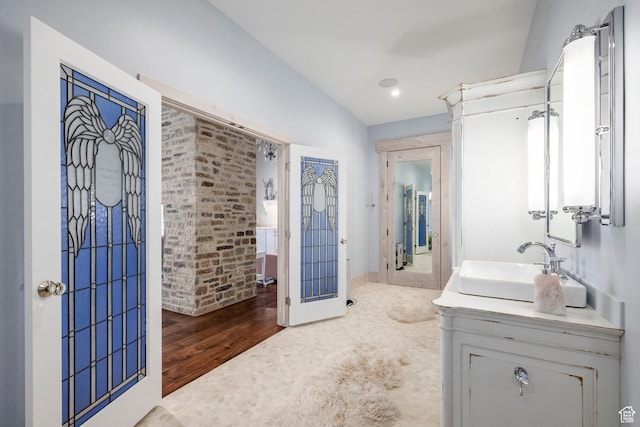 bathroom with vaulted ceiling, vanity, wood finished floors, baseboards, and recessed lighting