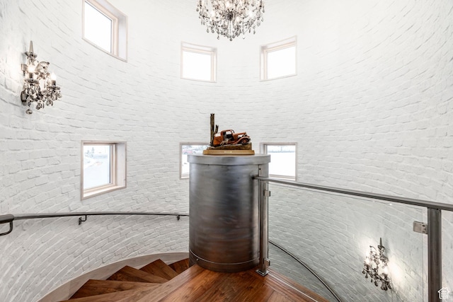 stairway featuring brick wall, a towering ceiling, a chandelier, healthy amount of natural light, and wood finished floors