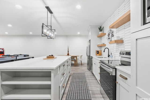 kitchen with decorative light fixtures, appliances with stainless steel finishes, white cabinetry, light hardwood / wood-style flooring, and a center island