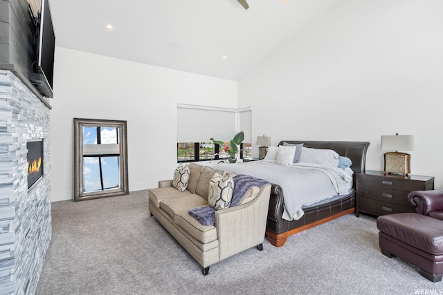 carpeted bedroom with high vaulted ceiling and a stone fireplace