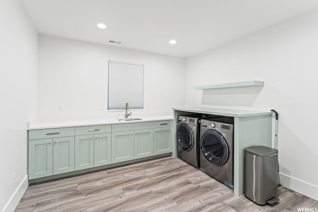 clothes washing area with separate washer and dryer, light hardwood / wood-style flooring, sink, and cabinets