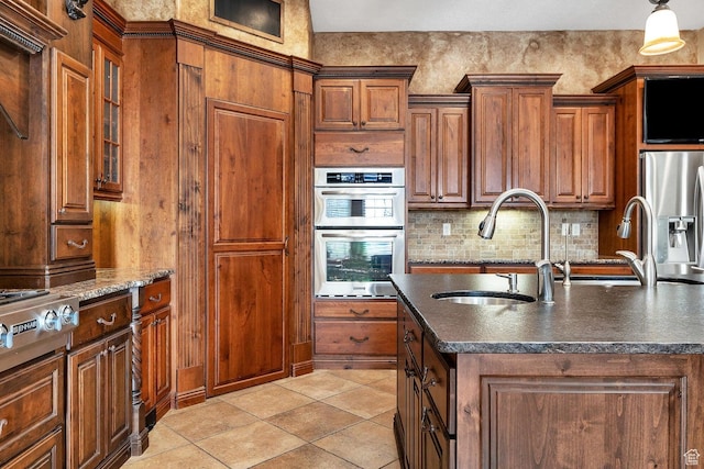 kitchen with a center island with sink, appliances with stainless steel finishes, sink, light tile patterned floors, and tasteful backsplash