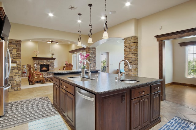 kitchen with sink, a center island with sink, stainless steel appliances, and a stone fireplace
