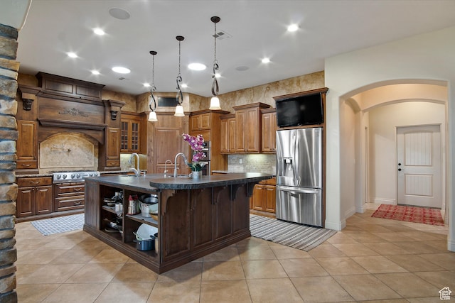 kitchen featuring a kitchen island with sink, decorative light fixtures, light tile patterned floors, appliances with stainless steel finishes, and a kitchen bar
