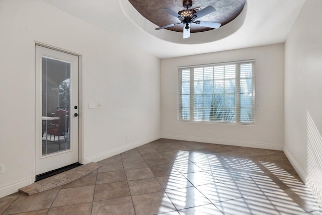 tiled empty room with ceiling fan and a tray ceiling