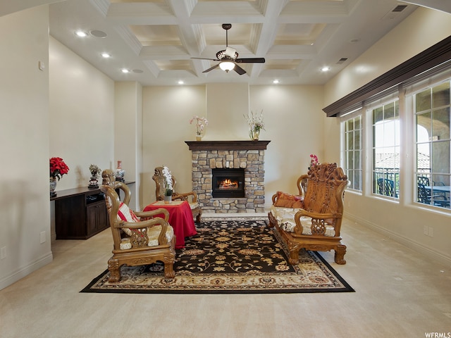 sitting room featuring coffered ceiling, a stone fireplace, ceiling fan, light colored carpet, and beam ceiling