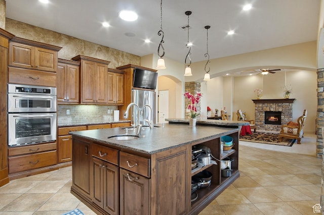 kitchen featuring hanging light fixtures, an island with sink, stainless steel appliances, a fireplace, and sink