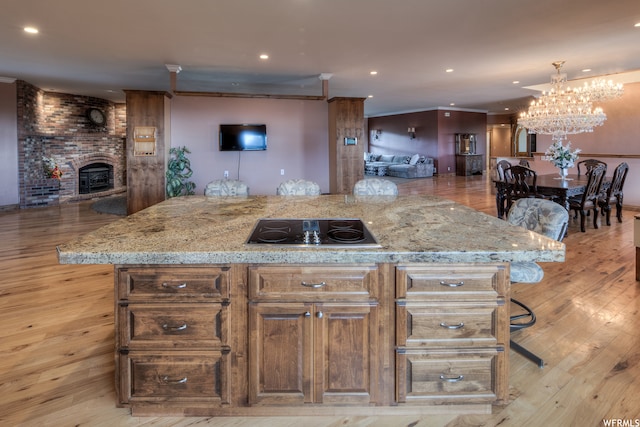 kitchen with an inviting chandelier, light hardwood / wood-style floors, black electric cooktop, and a fireplace