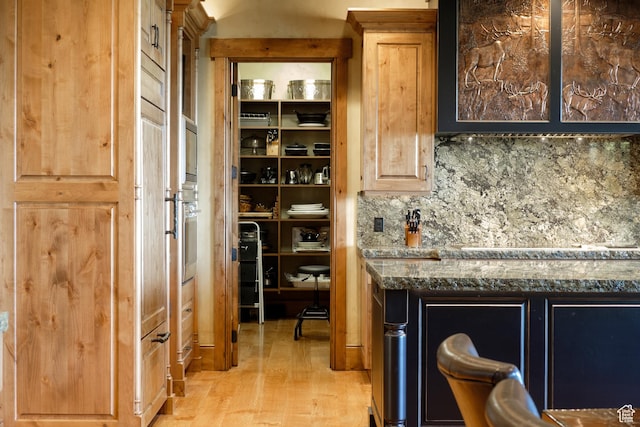 bar featuring decorative backsplash, light wood-style flooring, and stainless steel oven