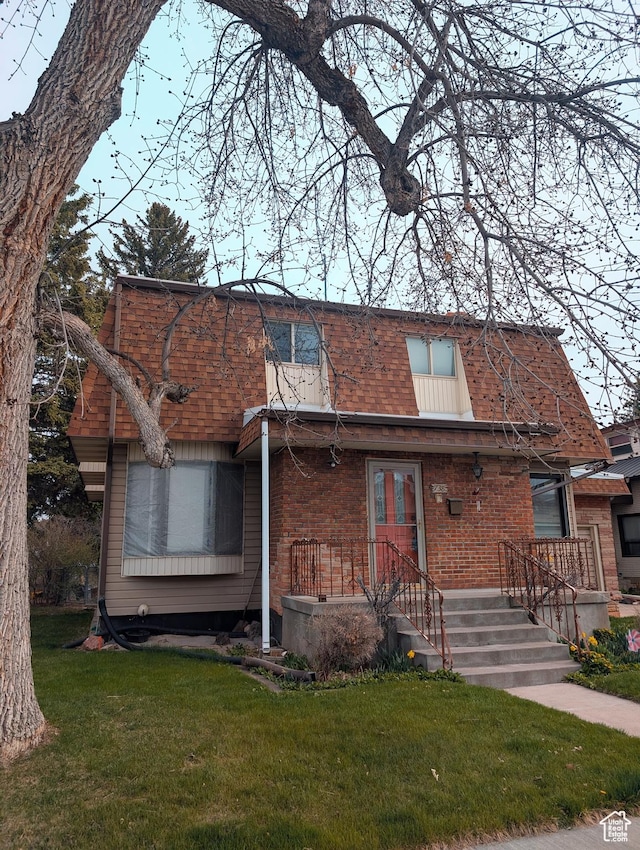 view of front facade featuring a front yard, roof with shingles, mansard roof, and brick siding