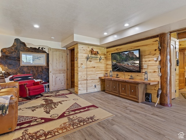living room with light hardwood / wood-style floors, a textured ceiling, and wood walls