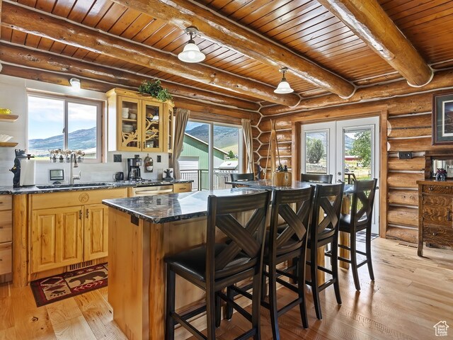 kitchen featuring light hardwood / wood-style floors, beamed ceiling, rustic walls, and a kitchen breakfast bar