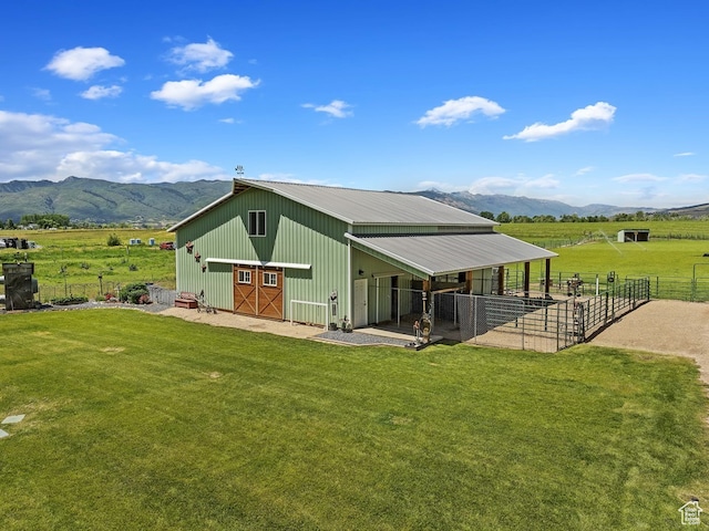 rear view of house featuring a yard, an outdoor structure, a mountain view, and a rural view