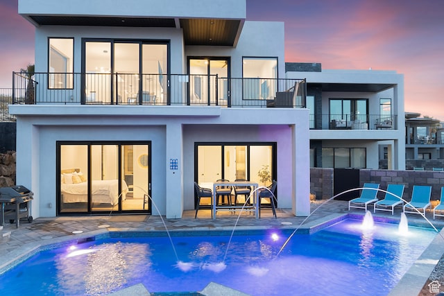 1560 W Torrey Pines Rd, Hurricane, UT 84737 - back house at dusk featuring a balcony, a patio, and pool water feature