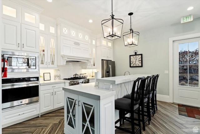 kitchen with appliances with stainless steel finishes, white cabinets, a center island, dark parquet flooring, and a breakfast bar area