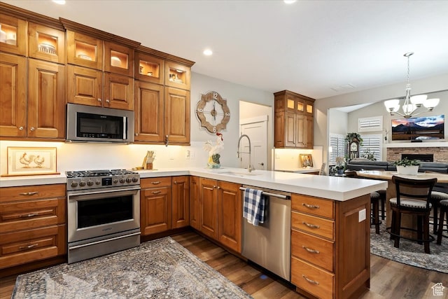 kitchen featuring appliances with stainless steel finishes, a chandelier, a stone fireplace, dark hardwood / wood-style floors, and hanging light fixtures